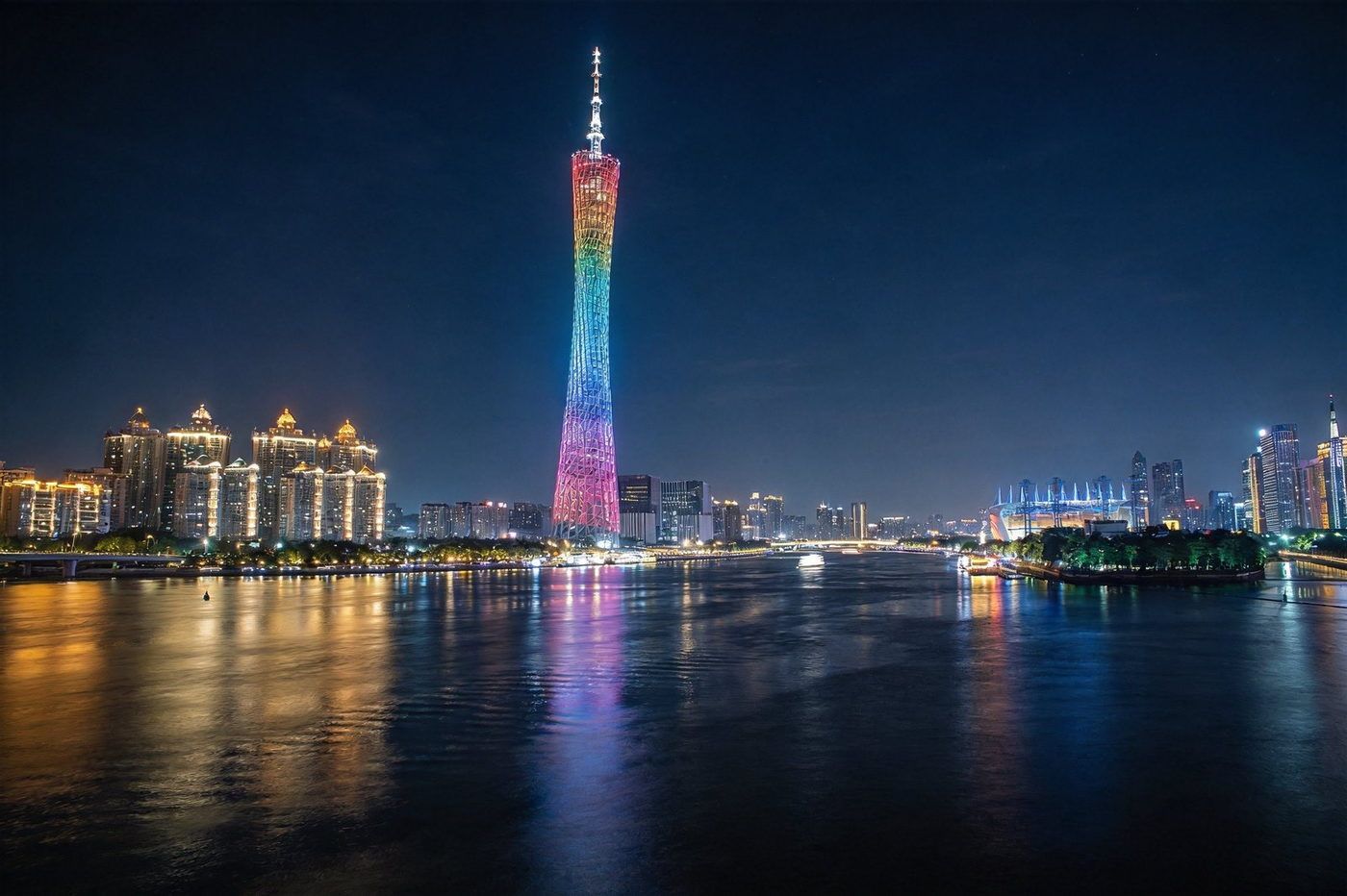 广州塔珠江夜景：珠江边矗立的多彩灯光广州塔（小蛮腰），夜景灯光璀璨通亮，倒影映在珠江江面，城市天际线