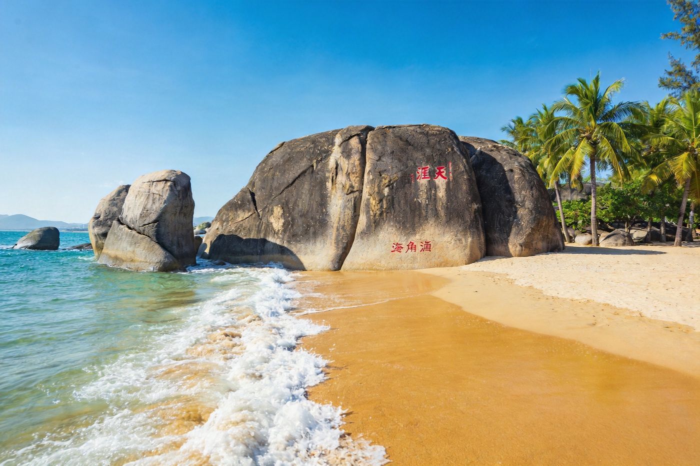 三亚天涯海角：海边矗立的巨大花岗岩礁石上刻红字，碧海蓝天、椰林沙滩环绕，海浪拍岸